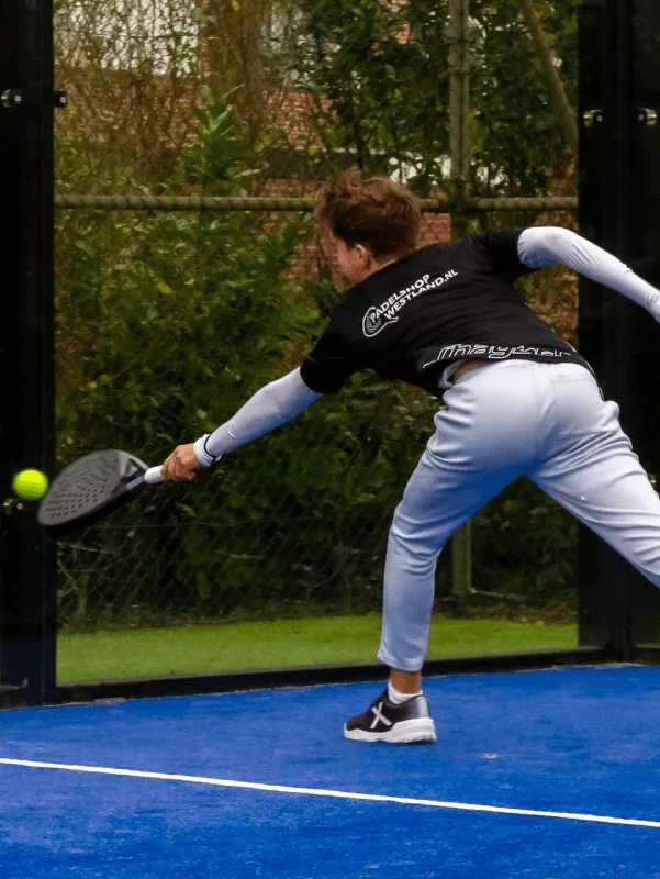 Padel speler in actie met een zwart padelracket op een blauwe buitenbaan | PadelShopWestland